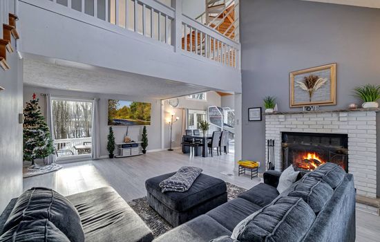 Spacious and inviting living area with a cozy fireplace, vaulted ceilings, and large windows offerin