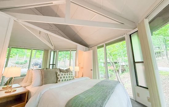Experience the unique architecture in this inviting bedroom, featuring vaulted ceilings and large windows that connect you with the beautiful surroundings.