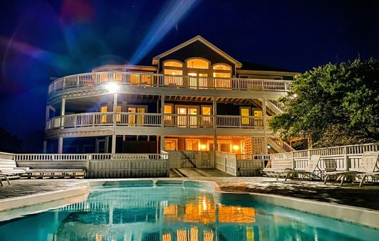 The Fitzgerald Estate illuminated at twilight — private heated pool, expansive multilevel decks, and direct oceanfront access for an unforgettable luxury retreat on the Outer Banks
