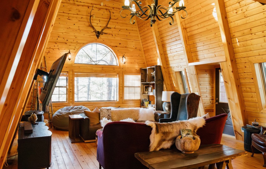 Spacious A-frame living room with dramatic vaulted ceilings, statement chandelier, and multiple seating areas—ideal for gathering, movie nights, and relaxing in a warm, rustic White Mountains cabin retreat.