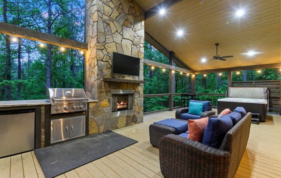 Generous back porch featuring cozy seating, a built-in grill, mini fridge, and inviting fireplace