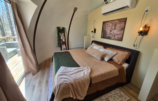 King bed with view out panoramic window to deck and woods beyond