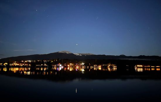 Lights from the far shoreline shimmer across the lake as the deep blue sky fades toward the horizon. The water reflects the quiet glow, creating a peaceful evening scene that feels calm, open, and still.