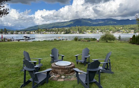 A wide, green backyard stretches to the lake, with a dock and fire pit ready for evenings outdoors. The open lawn feels inviting, and the calm water reflects the shoreline, creating a peaceful connection between land and lake.