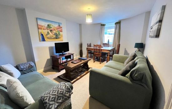 Open-plan living/dining - green sofas, dining table, flat-screen TV (angle 1)
