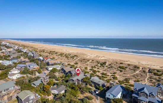 Sweeping coastal view over sandy shores, rooftops & endless ocean horizons.