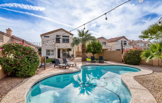 Resort style backyard with a sparkling pool and lounge seating under open skies.