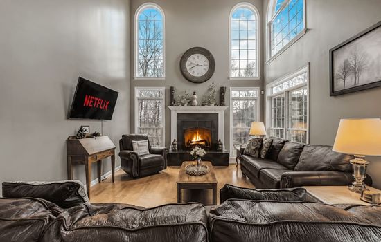 Grand living room with soaring ceilings, oversized windows, and a cozy stone fireplace.