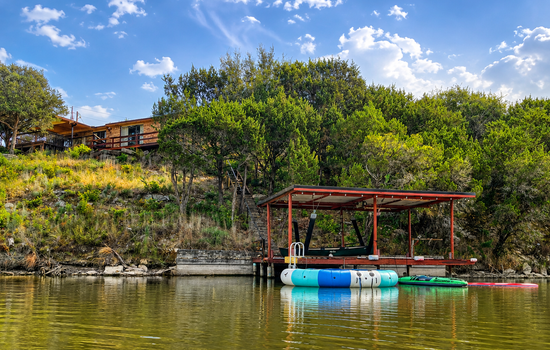 Private lakefront dock stocked for fun on the water, with life jackets, an inflatable trampoline, lily pad, inflatable kayak, canoe, and assorted inflatable tubes.